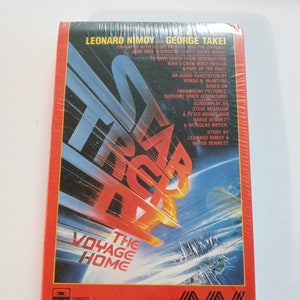 May include: Sealed cassette tape of "Star Trek IV: The Voyage Home." The cover features a red border with the title in large, stylized letters. The image shows a spaceship and a planet. The text includes the names Leonard Nimoy and George Takei.