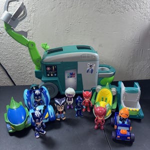 May include: A teal and green mobile command center toy with a large mechanical claw arm, accompanied by several small plastic character figurines and miniature vehicles, including blue, red, and green themed cars and various cartoon figures.