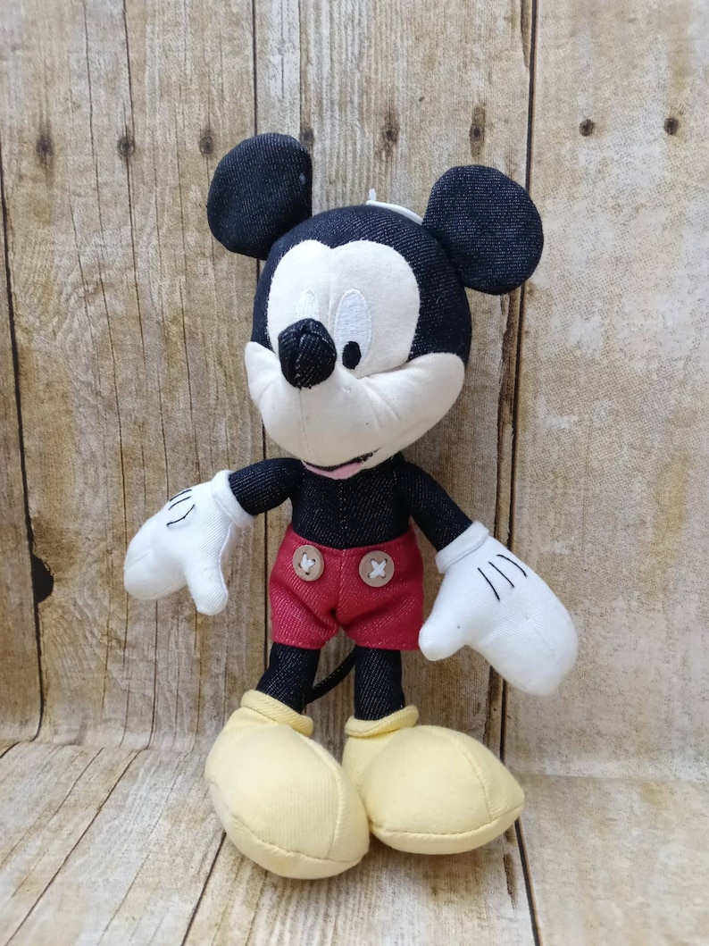 K&ouml;nnte beinhalten: Ein Mickey Mouse Stofftier mit schwarzen denimartigen Ohren, Kopf und Armen. Das Spielzeug hat ein wei&szlig;es Gesicht, H&auml;nde und gelbe Schuhe. Es tr&auml;gt rote Shorts mit zwei braunen Kn&ouml;pfen.