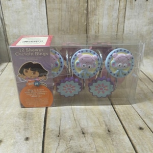 May include: A package of 12 Dora the Explorer shower curtain rings. The rings are pink and blue with a cartoon image of Dora and a flower design. The package says "12 Shower Curtain Rings".