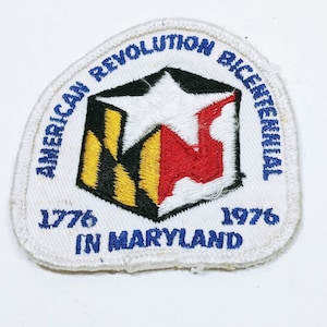 Puede incluir: Parche blanco bordado con costuras azules. El parche presenta una estrella roja, blanca y amarilla y el texto "American Revolution Bicentennial 1776 In Maryland 1976".