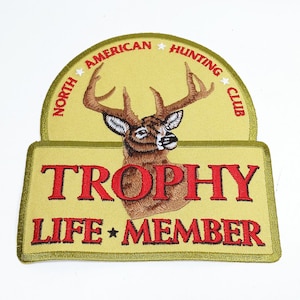 May include: A yellow and green embroidered patch with a white star and the text "North American Hunting Club". A brown deer head with antlers is in the center of the patch. Below the deer head is the text "Trophy Life Member" in red.