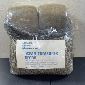 May include: A plastic-wrapped package of Seven Seas Supply Inc. Ocean Treasures Decor containing two tan fishing floats, a dark gray rope, and a tan fish net. The label states the net size is approximately 4' x 4' and includes fishing gear.