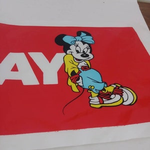 May include: A red poster with the word "AY" in white letters. The poster features a cartoon illustration of Minnie Mouse wearing a yellow dress, blue bow, and blue shoes.
