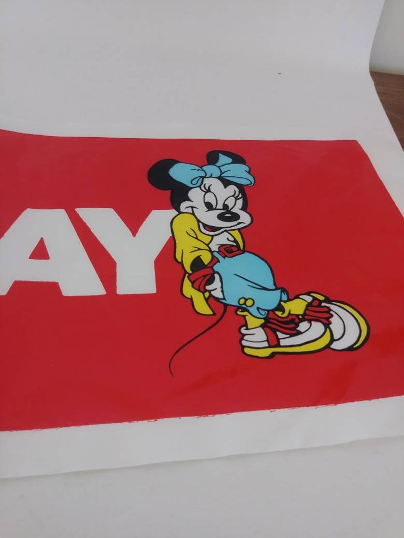 May include: A red poster with the word "AY" in white letters. The poster features a cartoon illustration of Minnie Mouse wearing a yellow dress, blue bow, and blue shoes.