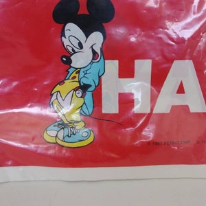 May include: A red plastic bag featuring a cartoon image of Mickey Mouse in a blue jacket and yellow shoes. The word "HA" is printed in white. The bag has a copyright notice from 1987.