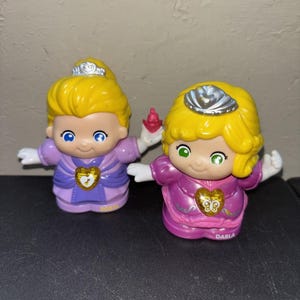 May include: Two plastic toy figures with yellow hair and silver crowns. The left figure, labelled Robin, wears a light purple dress with a gold heart emblem. The right figure, labelled Darla, wears a dark purple dress with a gold heart and butterfly emblem.