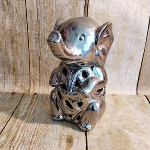 Peut inclure: Une figurine d'éléphant en céramique argentée avec un motif découpé décoratif. L'éléphant est assis, la trompe levée.