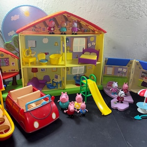 May include: A multi-level yellow plastic dollhouse with a red roof, featuring various rooms, furniture, and multiple small pig character figurines. Includes a red toy car, a yellow boat with a pirate flag, a green slide, and a swing set accessory.