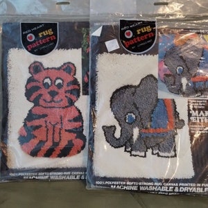 May include: Two Red Heart rug pattern kits in plastic packaging. One features a red and black tiger design, the other a gray elephant with a blue and orange harness. The packaging includes the text "100% Polyester Soft & Strong Rug Canvas".