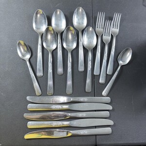 May include: A set of vintage cutlery, including spoons, forks, and knives. The spoons and forks feature a floral pattern on the handles, while the knives have a simple design. The silverware is arranged on a dark surface.