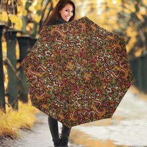 May include: A black umbrella with a colorful, intricate pattern of swirls and flowers in shades of yellow, orange, red, and pink. The umbrella is closed and held by a person.