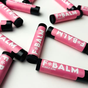 May include: Several pink lip balm tubes with black caps and white text that reads "F*BALM" and "BUBBLE GUM".
