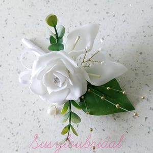 May include: White silk rose and calla lily buttonhole with gold and pearl accents and greenery.