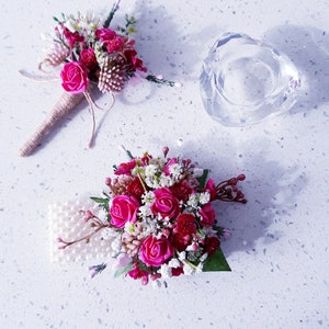 May include: Two pink and white flower bouquets with pearl accents. The bouquets are arranged on a white surface with a clear glass candle holder.