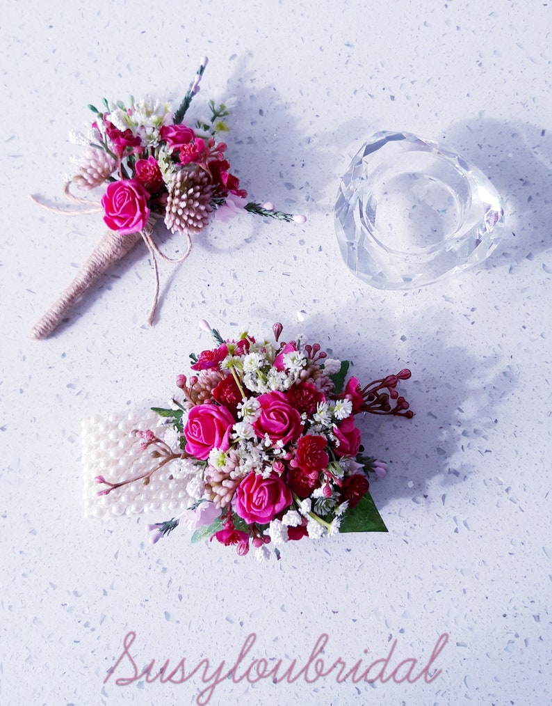 May include: Two pink and white flower bouquets with pearl accents. The bouquets are arranged on a white surface with a clear glass candle holder.