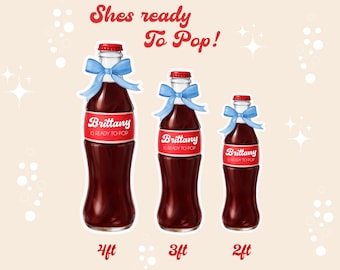Puede incluir: Tres botellas decorativas con etiquetas rojas que dicen "Brittany is ready to pop!" están atadas con lazos azules. Las botellas están etiquetadas 2ft, 3ft y 4ft. El texto "Shes ready To Pop!" está escrito en rojo.
