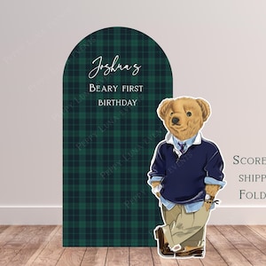Pode incluir: Um grande cenário em arco com um padrão xadrez verde e preto, com o texto "Beary First Birthday de Joshua". Uma figura de urso de camisola e cáqui está ao lado. As palavras "Scored & Shipped Folded" também são visíveis.