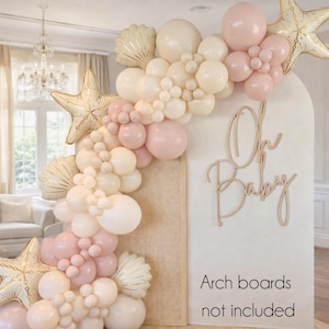 May include: A decorative balloon arch in shades of pink, cream, and gold, featuring star and seashell-shaped balloons. The arch is adorned with the words "Oh Baby" in wooden script, perfect for a baby shower or gender reveal party.