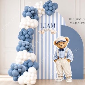 Può includere: Uno sfondo ad arco a righe blu e bianche con il nome LIAM e Est. 2024, decorato con una ghirlanda di palloncini blu e bianchi. Una sagoma di un orsacchiotto con berretto, camicia blu, papillon e pantaloni beige si trova davanti.