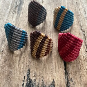 K&ouml;nnte beinhalten: F&uuml;nf bunte geh&auml;kelte Ringe mit verschiedenen Mustern. Die Ringe sind aus verschiedenen Farben gefertigt, darunter Braun, Blau, Grau, Beige und Rot.