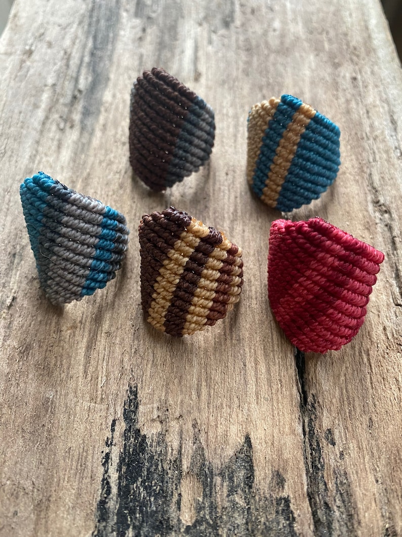 K&ouml;nnte beinhalten: F&uuml;nf bunte geh&auml;kelte Ringe mit verschiedenen Mustern. Die Ringe sind aus verschiedenen Farben gefertigt, darunter Braun, Blau, Grau, Beige und Rot.