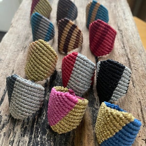 May include: A collection of 12 colorful, handmade friendship bracelets with various patterns and colors, including gold, silver, red, pink, blue, black, and brown. The bracelets are made with a braided cord and have a unique, geometric design.