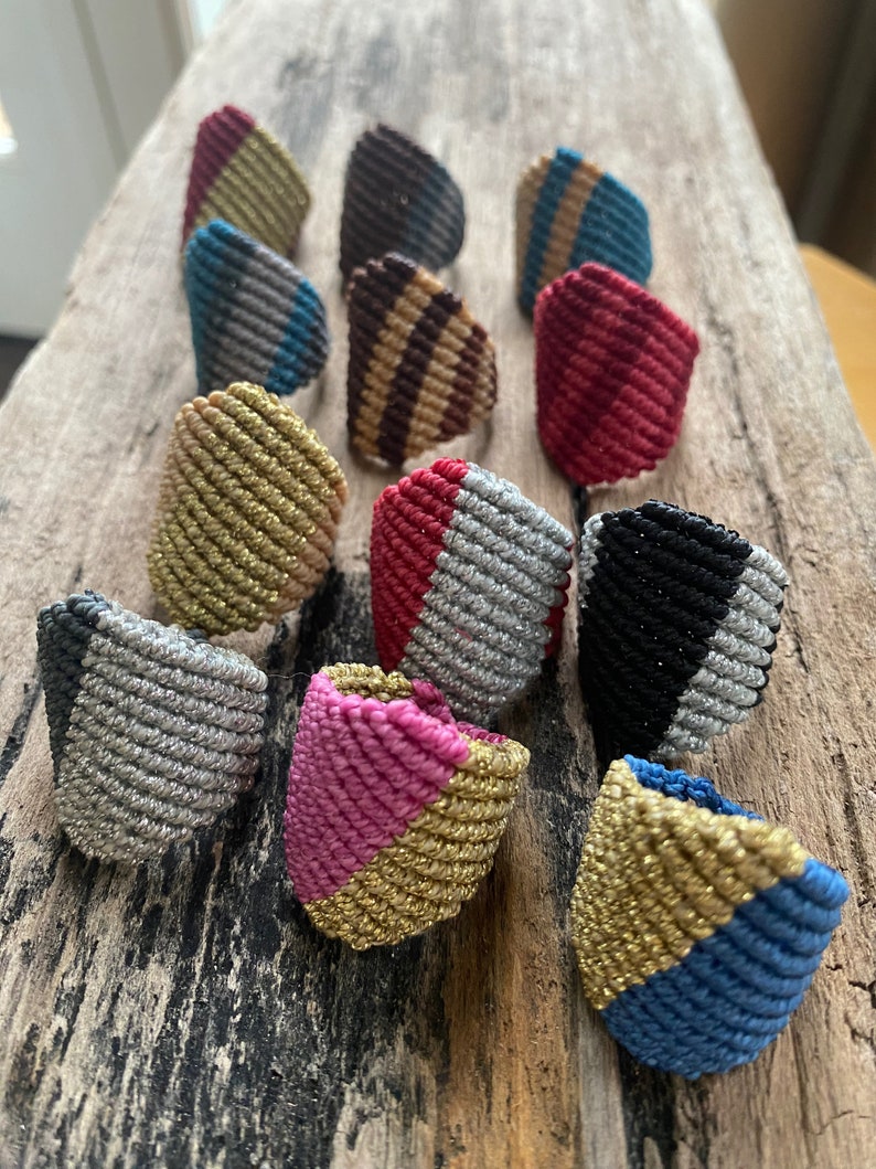 K&ouml;nnte beinhalten: Eine Sammlung von 12 bunten, handgefertigten Freundschaftsarmb&auml;ndern mit verschiedenen Mustern und Farben, darunter Gold, Silber, Rot, Pink, Blau, Schwarz und Braun. Die Armb&auml;nder sind aus geflochtener Schnur gefertigt und haben ein einzigartiges, geometrisches Design.