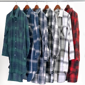 May include: Six plaid shirts hanging on wooden hangers on a silver rack. The shirts are in various colors, including green, blue, white, and red.