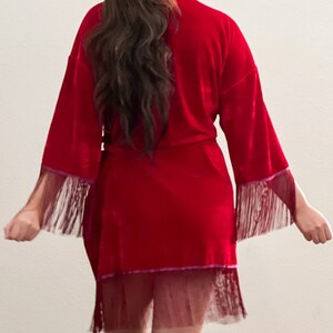 May include: A red velvet robe with a fringe trim and a sheer lace overlay. The robe has a tie closure at the waist.