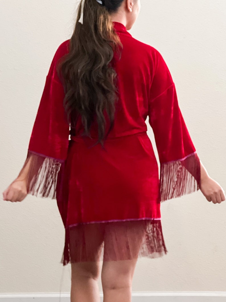 May include: A red velvet robe with a fringe trim and a sheer lace overlay. The robe has a tie closure at the waist.