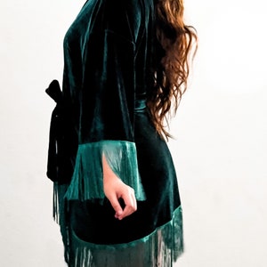 May include: A dark green velvet robe with a black sash and fringe trim. The robe has long sleeves and a relaxed fit.