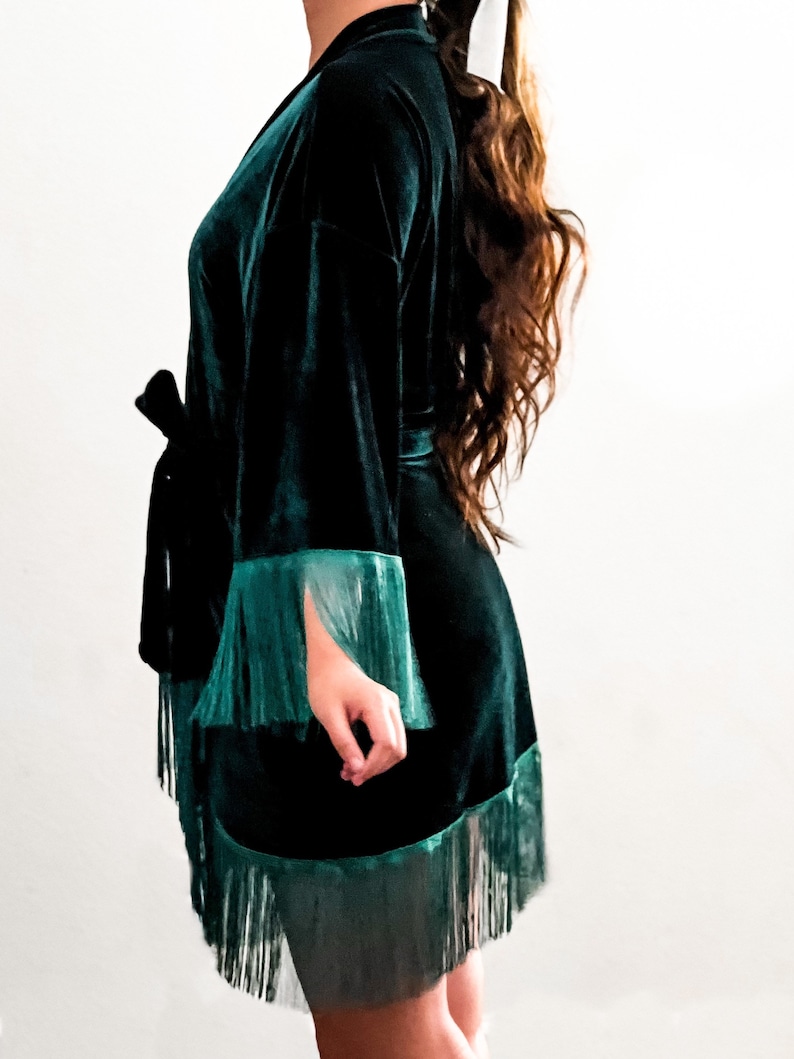 May include: A dark green velvet robe with a black sash and fringe trim. The robe has long sleeves and a relaxed fit.