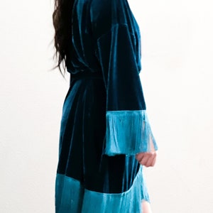 May include: A teal blue velvet robe with a fringe trim around the sleeves and hem.