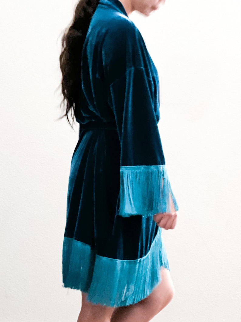 May include: A teal blue velvet robe with a fringe trim around the sleeves and hem.