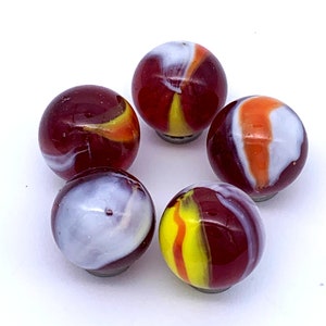 May include: Six glass marbles with red, white, and yellow swirling patterns. The marbles are arranged in a circle on a white surface.