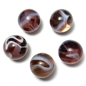 May include: Five glass marbles with swirling patterns of white and shades of brown and purple. The marbles are round and have a glossy finish, set against a white background. The marbles vary in their internal designs.