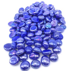 May include: A pile of iridescent blue glass pebbles. The pebbles are smooth and oval-shaped. They are perfect for adding a touch of sparkle to any home decor project.