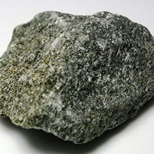 May include: A close-up of a rough, gray and green rock with a slightly textured surface.