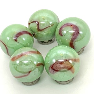 May include: Five green glass marbles with red and brown swirling patterns. The marbles are arranged in a circle.
