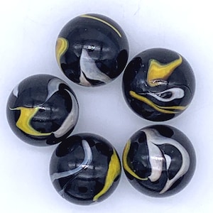May include: Six black marbles with yellow and white swirling patterns. The marbles are arranged in a circle on a white surface.