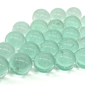 May include: A collection of translucent green glass marbles. The marbles are arranged in a triangular pattern on a white background.
