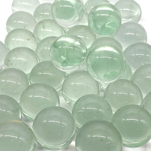 May include: A collection of translucent green glass marbles. The marbles are smooth and round, and they have a slight shimmer to them.