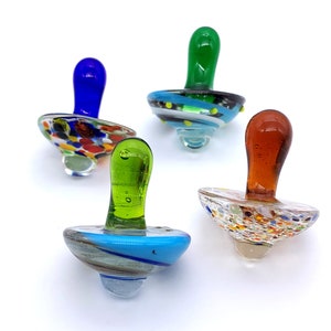 May include: Four colorful glass spinning tops with different designs. Each top has a round base and a pointed top. The tops are blue, green, red, and brown with white and yellow accents.