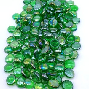 May include: A large pile of iridescent green glass pebbles. The pebbles are smooth and round, and they have a slight shimmer to them.
