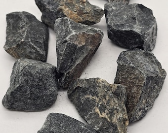 May include: A collection of rough-hewn, dark gray rocks with varying sizes and textures. Some rocks have patches of brown and tan hues, adding visual interest. The stones are scattered, suggesting a natural, earthy aesthetic, suitable for landscaping or decorative purposes.