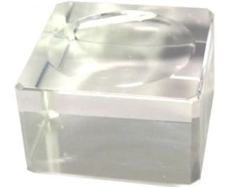 May include: A clear glass display stand with a square base and a raised circular platform. The stand is perfect for displaying small objects, such as figurines, jewelry, or coins.