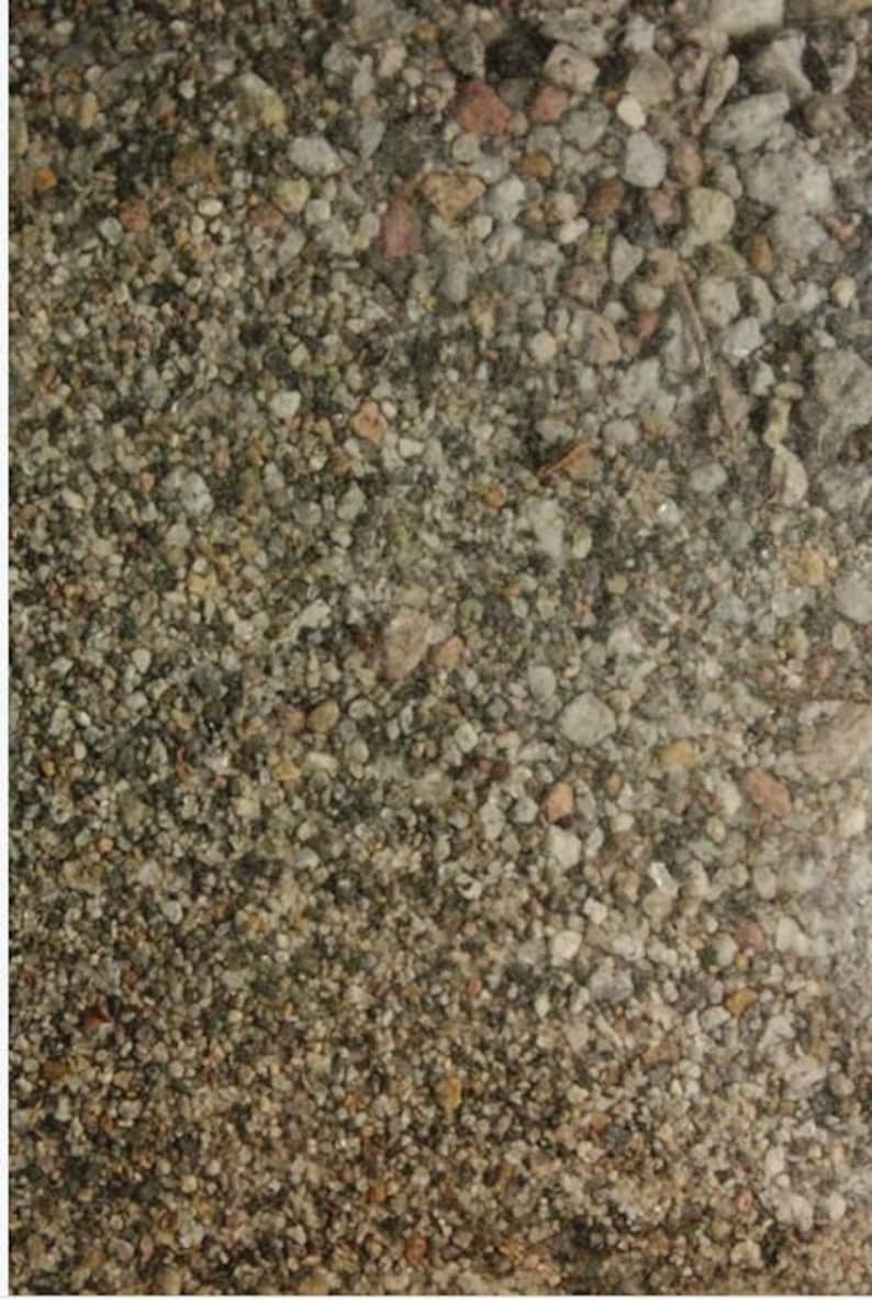 May include: A close-up of a variety of small, gray, brown, and white stones. The stones are tightly packed together, creating a textured surface.