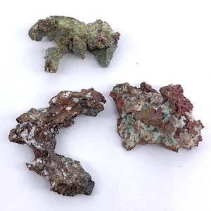 May include: Three pieces of raw copper ore with green, red, and white mineral deposits. The copper ore is rough and has an irregular shape.