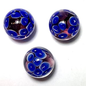 May include: Three glass marbles with a purple and white swirl pattern and blue spots.